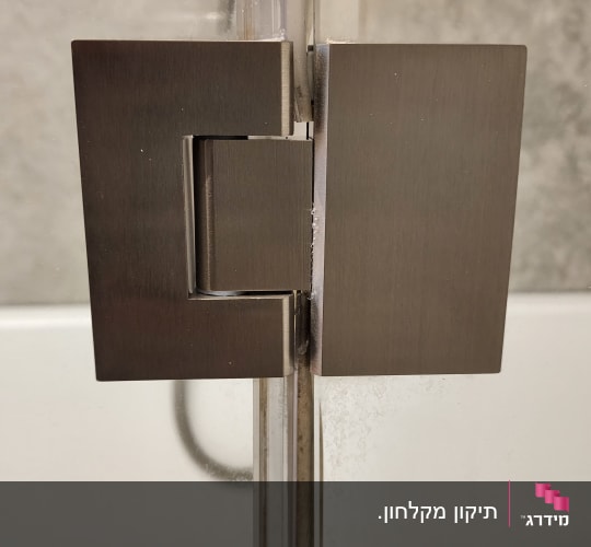 תקריב של ציר מתכת כהה המותקן על זכוכית מקלחון